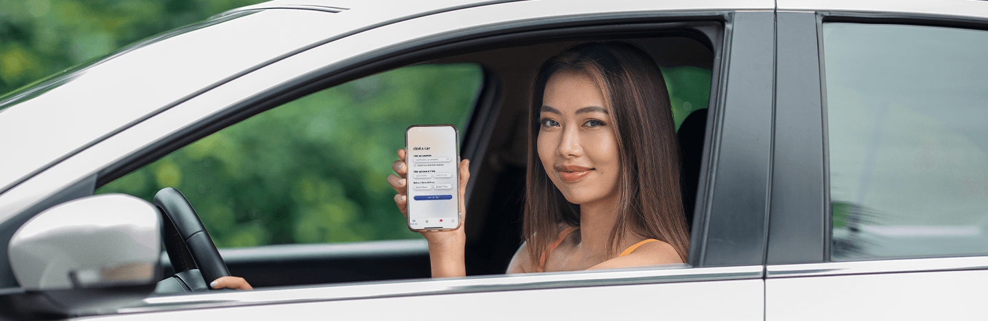 Happy woman sitting in a car and showing Yoma Car Share 2.0 app on mobile phone